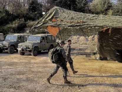 Dos de los soldados pasando por delante de los veh&iacute;culos y la carpa mimetizada.