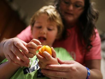 Un niño con leucodistrofia metacromática intenta pelar una mandarina con ayuda de su madre en su casa en Payson, Illinois (EE UU).
