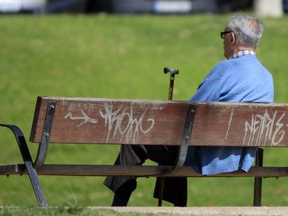 Un jubilado sentado con su bast&oacute;n en un banco de un parque.