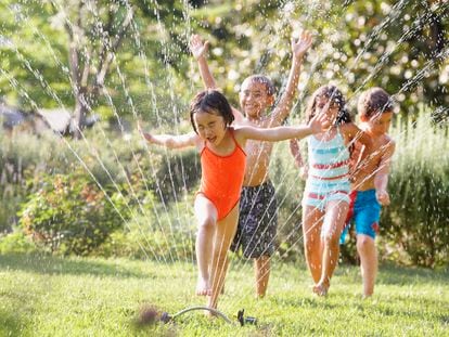 Varios niños juegan y se mojan con los aspersores de un jardín.