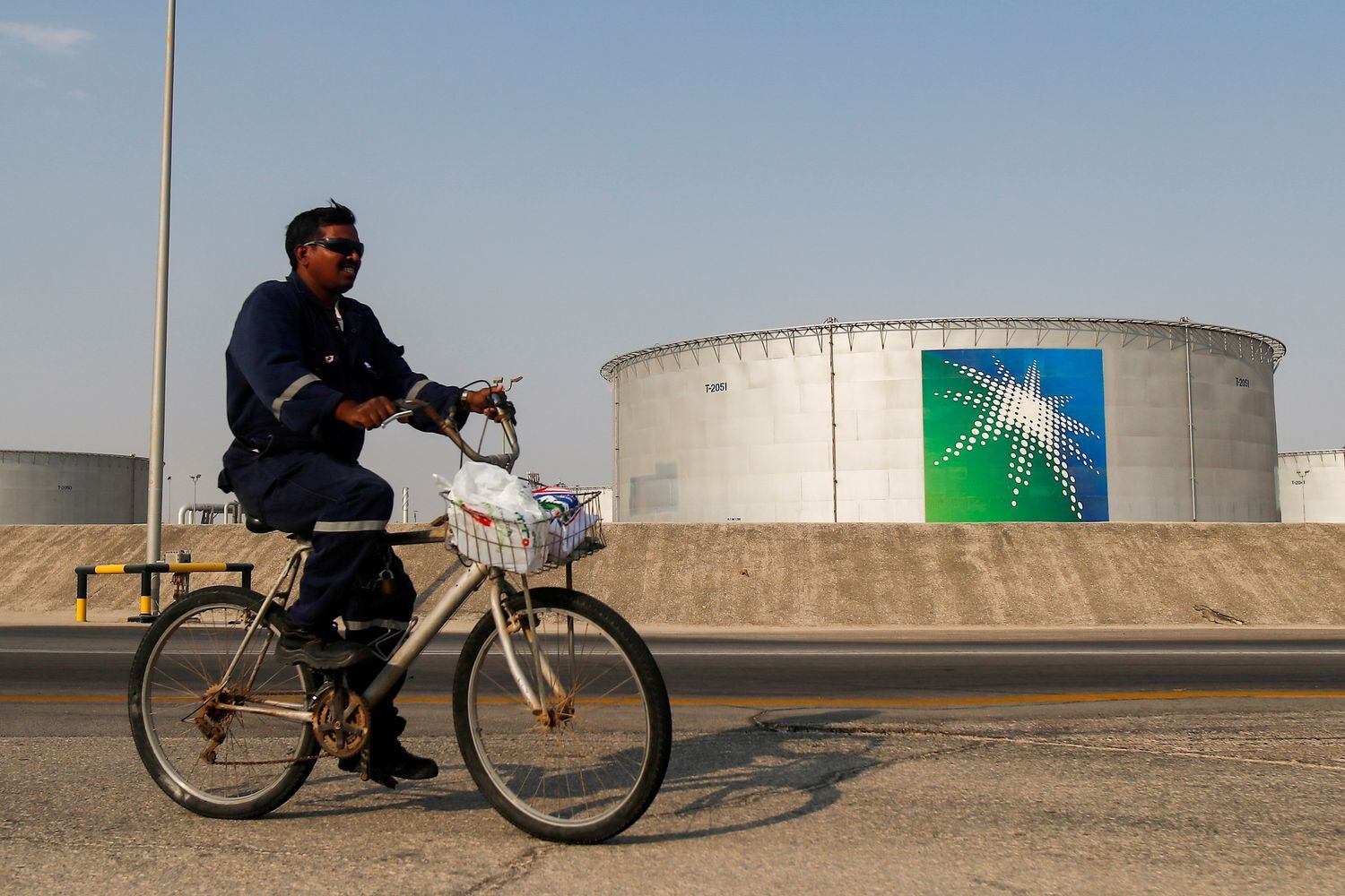 Un empleado pasa en bicicleta cerca de un tanque de petróleo de Aramco, la petrolera estatal saudí.