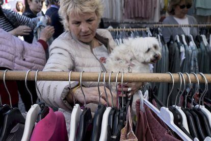 Una mujer ojea varias prendas con su perro en brazos en el mercadillo de Majadahonda.