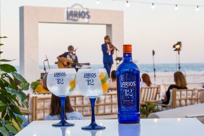 Una botella de la ginebra Premium Larios 12. Al fondo, La Bien Querida durante su conciertos en los Atardeceres Larios.