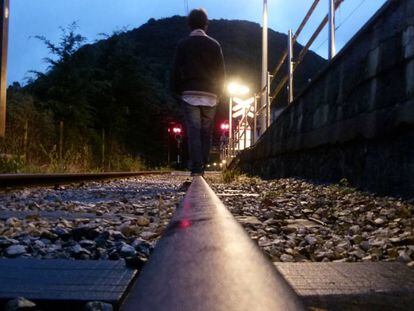 Un adolescente camina por una vía del tren. En vídeo, reportaje sobre el teléfono de atención al suicidio.