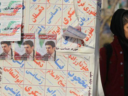 Una mujer iran&iacute; junto a los carteles electorales para los comicios de marzo.