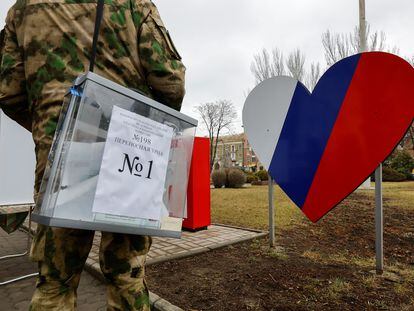 Un miembro en uniforme militar de la comisión electoral del territorio ocupado de Donetsk transporta una urna en un punto de voto situado en plena calle.