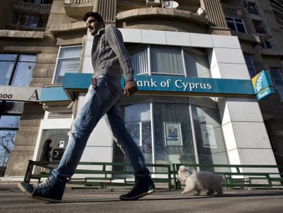 Un hombre pasa con su perro ante una sede del Banco de Chipre.