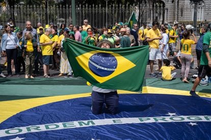 Un seguidor del presidente alza al cielo una bandera brasileña mientras está hincado sobre otra, durante las celebraciones por el día de la Independencia en Belo Horizonte.