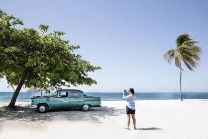 Una mujer fotograf&iacute;a un coche antiguo en una playa de Cuba. 