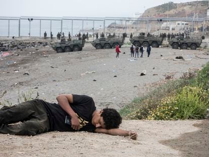 Una persona descansa en el suelo este martes en Ceuta, con tropas españolas desplegadas en la frontera, al fondo.