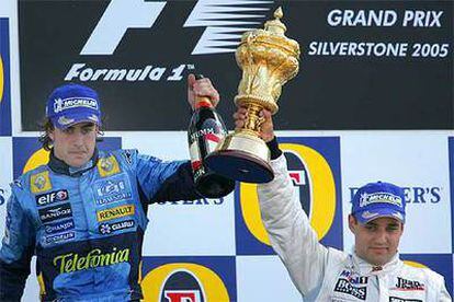 Fernando Alonso levanta una botella de cava mientras Juan Pablo Montoya alza su trofeo de vencedor en el circuito de Silverstone.