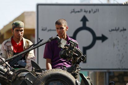 Dos rebeldes esperan en una carretera con un señal detrás donde puede leerse Trípoli, Zauiya y Subrata