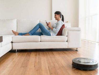 Una usuaria utiliza su móvil mientras un robot aspirador limpia la casa.