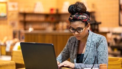 Una joven trabaja en una cafetería con su ordenador portátil y un teléfono móvil.