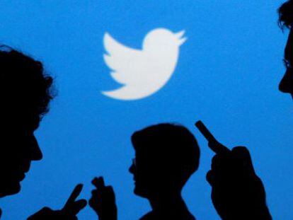 People holding mobile phones are silhouetted against a backdrop projected with the Twitter logo  in Warsaw
