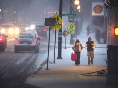 Tres personas caminan por la acera y varios coches circulan por la carretera en una tormenta invernal, el 22 de diciembre de 2022, en Chicago.
