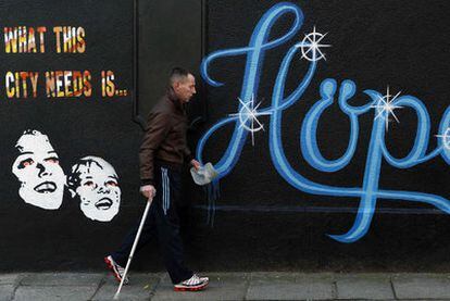 Un hombre camina por una calle de Dublín. En el muro se lee la frase "lo que esta ciudad necesita es... esperanza".