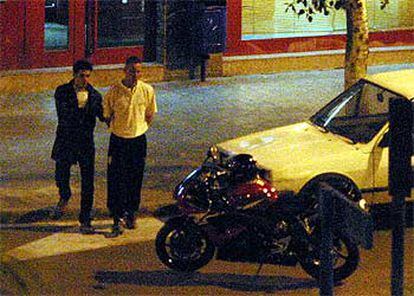 El atracador, vestido con ropa oscura, camina detrás del rehén hacia la moto en la que huyó antes de ser detenido.