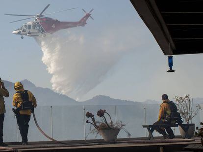 Los bomberos observan cómo un helicóptero arroja agua en un incendio forestal en el área de Pacific Palisades de Los Ángeles.