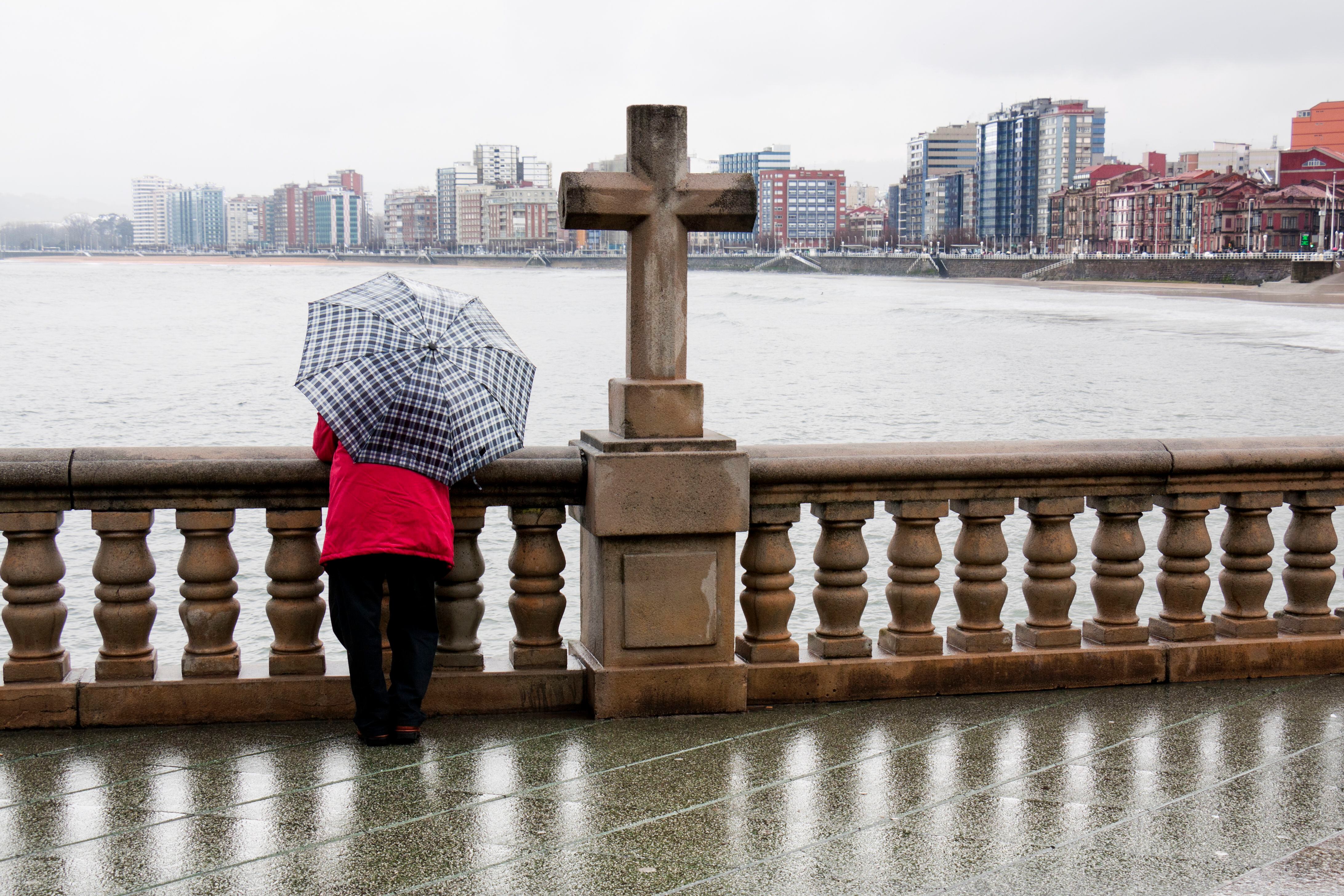 Una mujer con paraguas en un día de lluvia en la playa de San Lorenzo, en Gijón (Asturias).