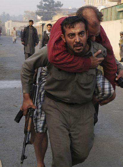 Un policía afgano acarrea a un herido en el asalto a la pensión donde se aloja personal de la ONU.