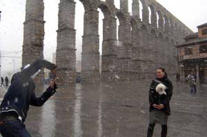 Varios turistas se fotografían en medio de una nevada junto al acueducto romano en la capital segoviana. EFE/Archivo