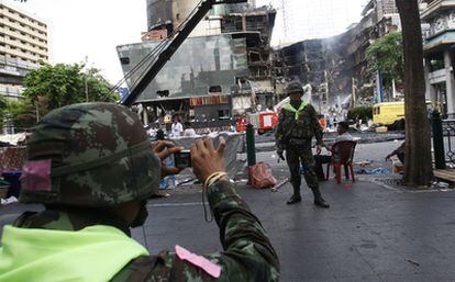 Un soldado tailandés saca una foto de un compañero ante el Central World, el segundo mayor centro comercial de Asia, destruido tras ser incendiado durante los disturbios del miércoles en Bangkok.
