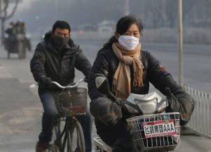 Una mujer china (dcha) se desplaza en bicicleta eléctrica y un hombre (izq) en bicicleta normal por Pekín.