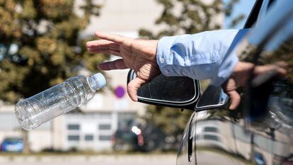 Un hombre arroja una botella de plástico vacía por la ventanilla de su coche.
