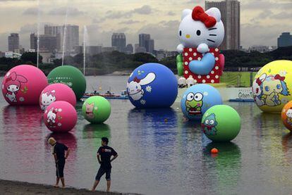 Dos jóvenes contemplan la Hello Kitty gigante y los globos con otros personajes de la compañía Sanrio en la bahía de Tokio.