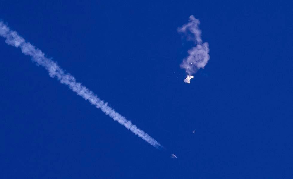 In this photo provided by Chad Fish, the remnants of a large balloon drift above the Atlantic Ocean, just off the coast of South Carolina, with a fighter jet and its contrail seen below it, Saturday, Feb. 4, 2023. The downing of the suspected Chinese spy balloon by a missile from an F-22 fighter jet created a spectacle over one of the state's tourism hubs and drew crowds reacting with a mixture of bewildered gazing, distress and cheering. (Chad Fish via AP)