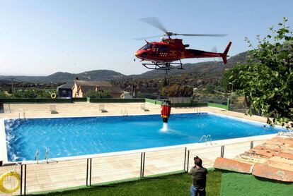 Un helicóptero de Bomberos de Madrid recoge agua de una piscina en el término municipal de Cadalso de los Vidrios, Madrid.