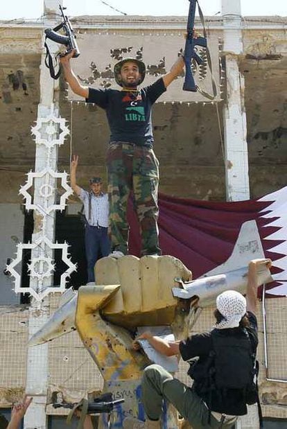 Un rebelde celebra la toma de Bab al-Aziziya, residencia de Gadafi, subido sobre la estatua de un puño de oro que rompe un avión estadounidense, símbolo del regimen.