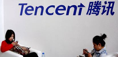 Dos mujeres juegan en su telefono m&oacute;vil bajo un cartel de la empresa Tencent.