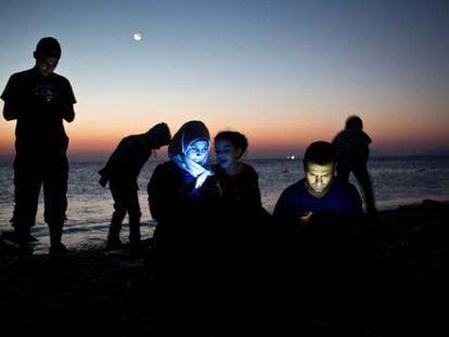 Un grupo de refugiados consulta sus m&oacute;viles a su llegada en barca a la isla griega de Kos.