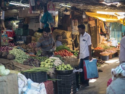 Un hombre con una bolsa de tela para hacer la compra adquiere legumbres en un mercado de Bombay.