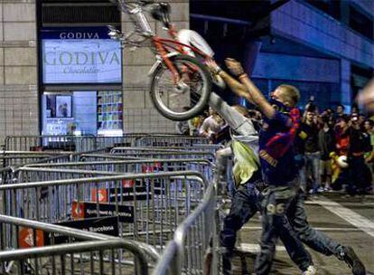 Dos alborotadores lanzando una bicicleta por encima de las vallas dipuestas por la policía para limitar las agresiones.