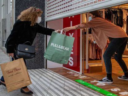 Una clienta recoge una bolsa de manos de una dependienta en un comercio del centro de Barcelona, este jueves en Cataluña.  