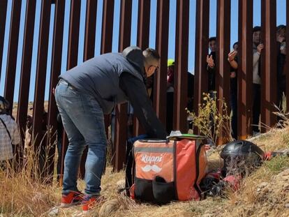 Un repartidor de comida entrega alimentos a migrates que esperan del otro lado del muro fronterizo en Tijuana, México, el 10 de mayo 2023.