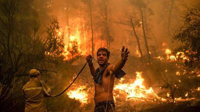 Un residente local hace un gesto mientras sostiene una manguera de agua vacía durante un intento de extinguir los incendios forestales que se acercan al pueblo de Pefki en la isla de Evia (Eubea), Grecia.