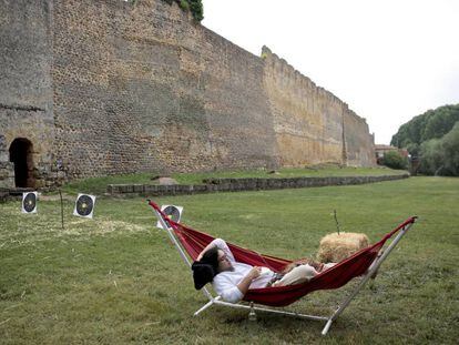 Un hombre con vestimenta medieval descansa frente a las murallas de Mansilla de las Mulas durante una celebración de feria medieval.