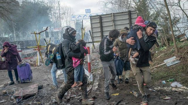 Unos padres protegen a sus hijos de los botes lacrimógenos lanzados por la policía griega, este sábado en Pazarkule.