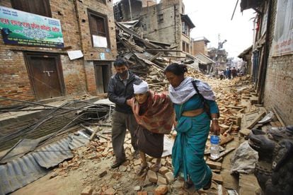 Una anciana camina, ayudada por dos personas, por las calles de Bhaktapur, cerca de Kathmandu, tras tener que abandonar su casa.