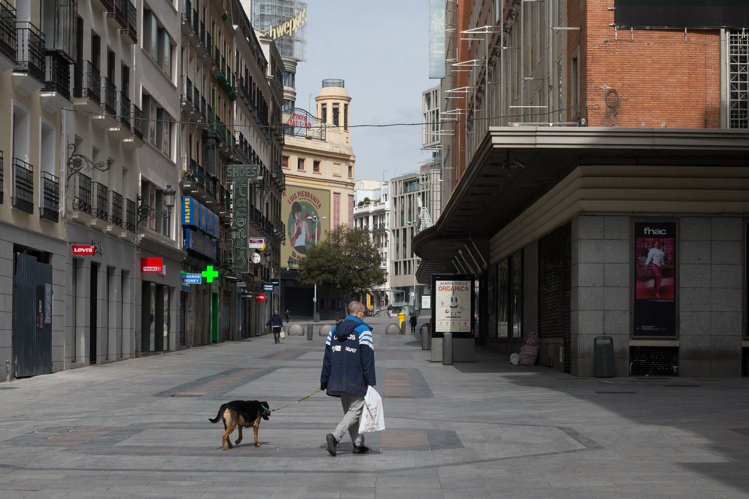 Un hombre pasea a su perro por la céntrica calle de Preciados, durante el estado de alarma.