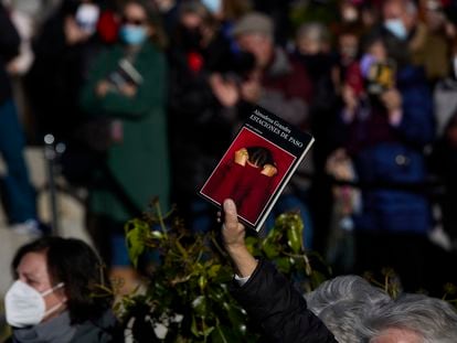 Un asistente al entierro de Almudena Grandes, este lunes en Madrid, levanta un ejemplar de su libro de cuentos 'Estaciones de paso'.