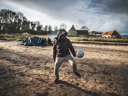 Un joven juega al fútbol en un campamento improvisado en la periferia de Calais (Francia), donde migrantes de diversas nacionalidades aguardan para intentar alcanzar el Reino Unido.