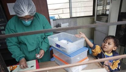Un ni&ntilde;o con tuberculosis tiende la mano para coger las p&iacute;ldoras de pie junto a una enfermera en un puesto de salud en las afueras de Lima (Per&uacute;)