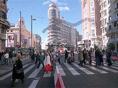 Decenas de peatones cruzan la Gran Vía, a la altura de la plaza del Callao, en el último domingo navideño de cortes de tráfico.
