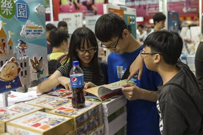Varios jóvenes ojean un libro en la 27ª edición de la feria del libro de Hong Kong