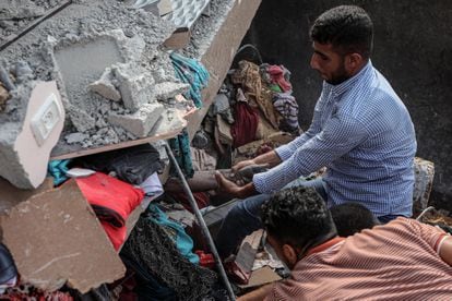 Una palestino intenta rescatar el cadáver de una persona atrapada entre los escombros de un edificio destruido tras un bombardeo israelí en Khan Yunis, este domingo.